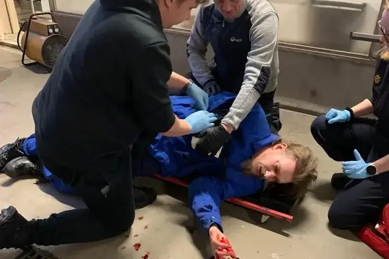 Kolme ihmistä harjoittelemassa elvytystä ensiaputilanteessa lattialla makaavalle potilaalle.